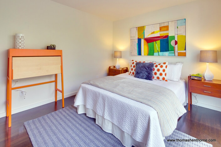 Bed in bedroom with grey area carpet over wood