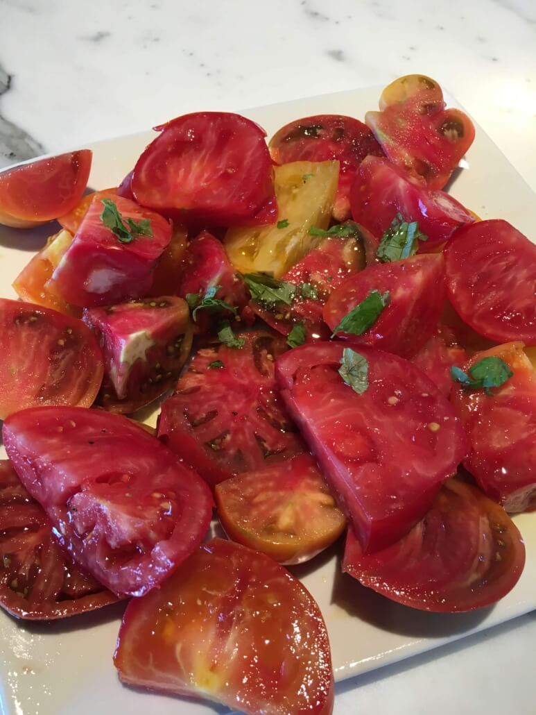 Plate of sliced tomatoes with salt and basil and olive oil