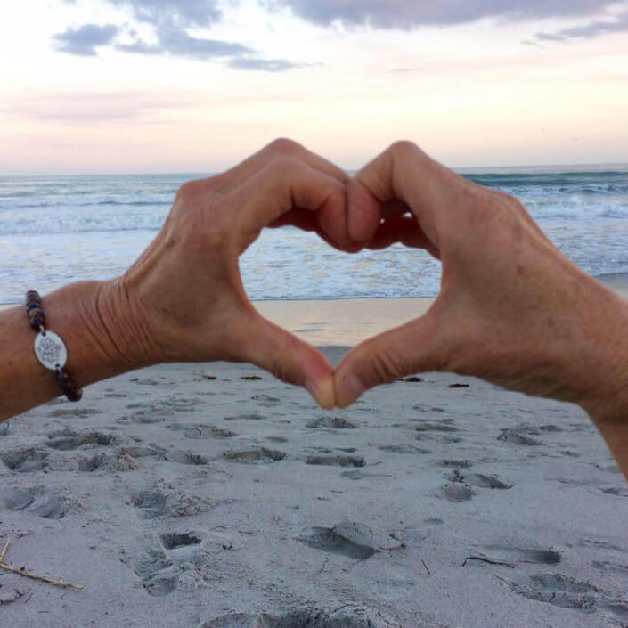 Sukha Yoga hands forming a heart on a beach