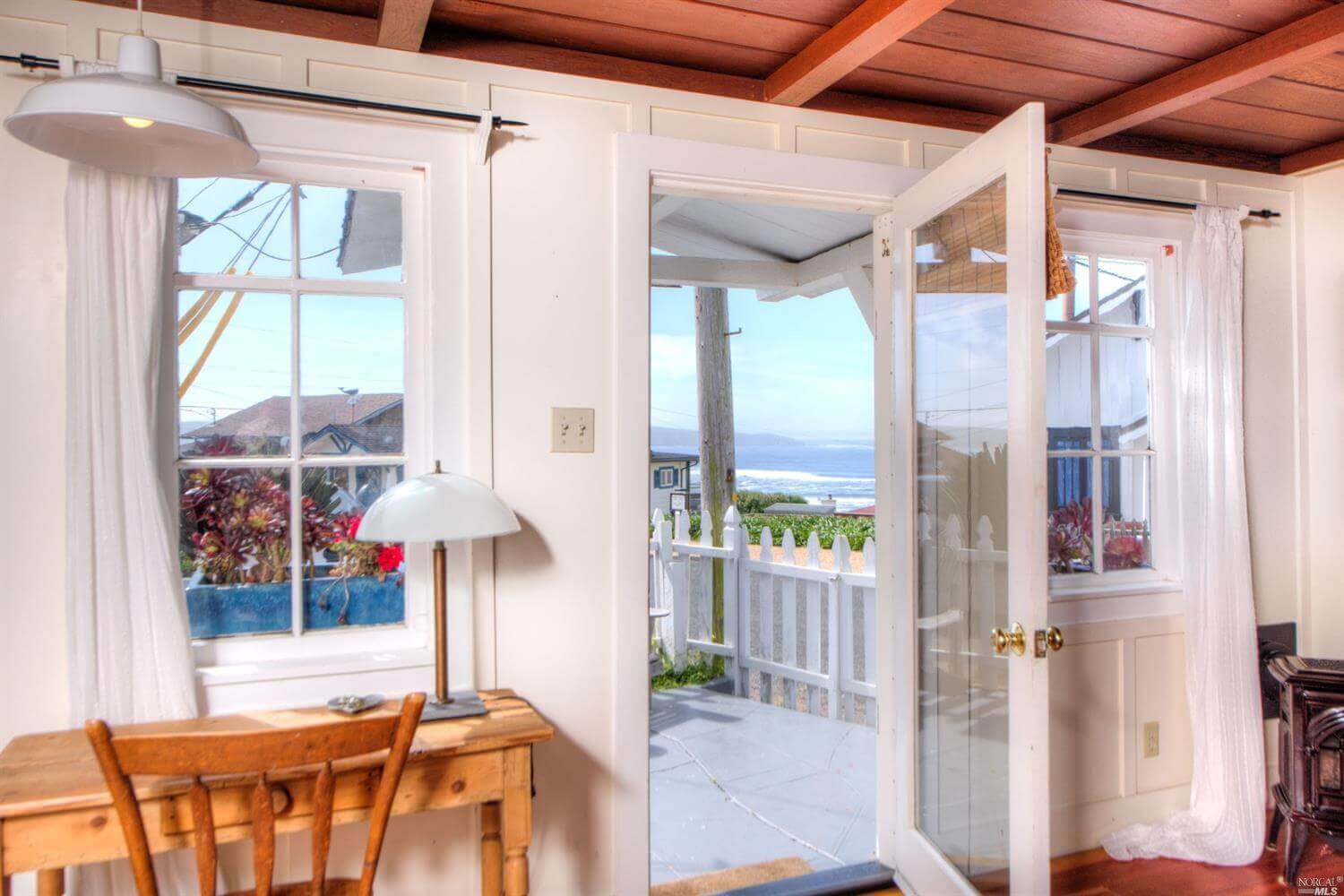 Door of cottage open looking to white picket fence and ocean in distance