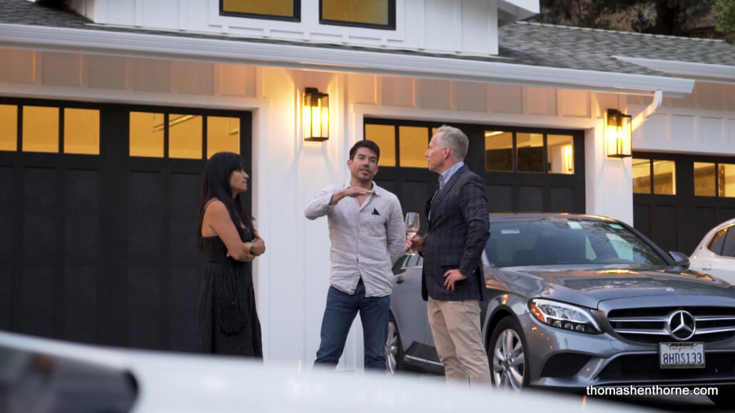 Two men and a woman talking next to a Mercedes in front of a garage