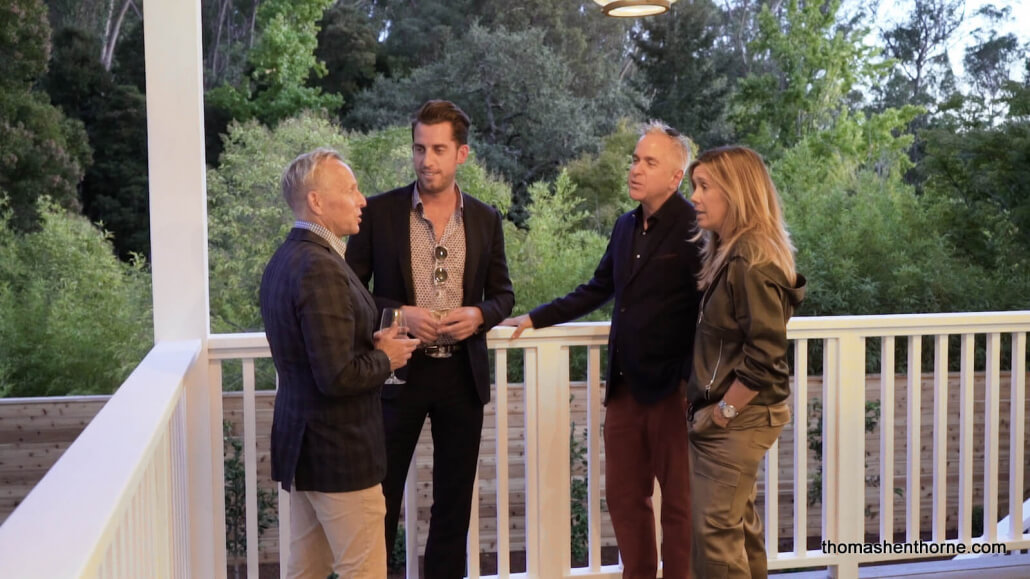 Three men and a woman talking on a front porch