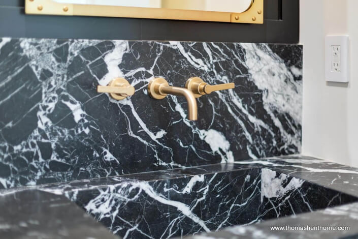 close up of marble sink with gold colored faucet and handles