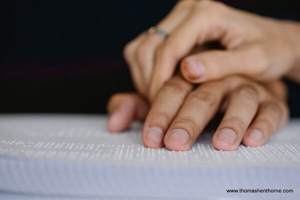 Photo of two people holding hands on a braille book